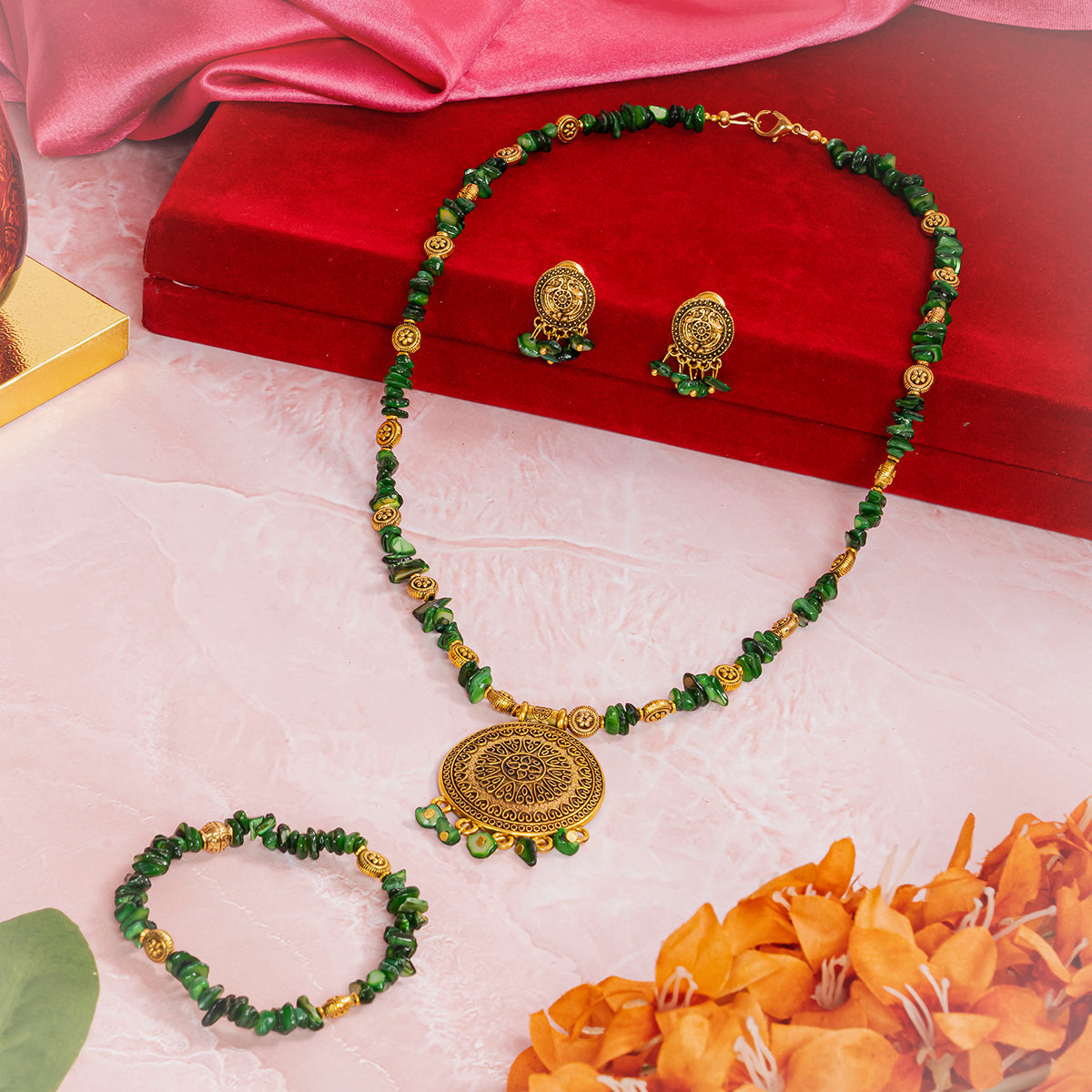 Eykaa GREEN MOTHER OF PEARL WITH GOLDEN CHARMS AND PENDANT BRACELET beside red velvet box, silky pink fabric, and orange flowers