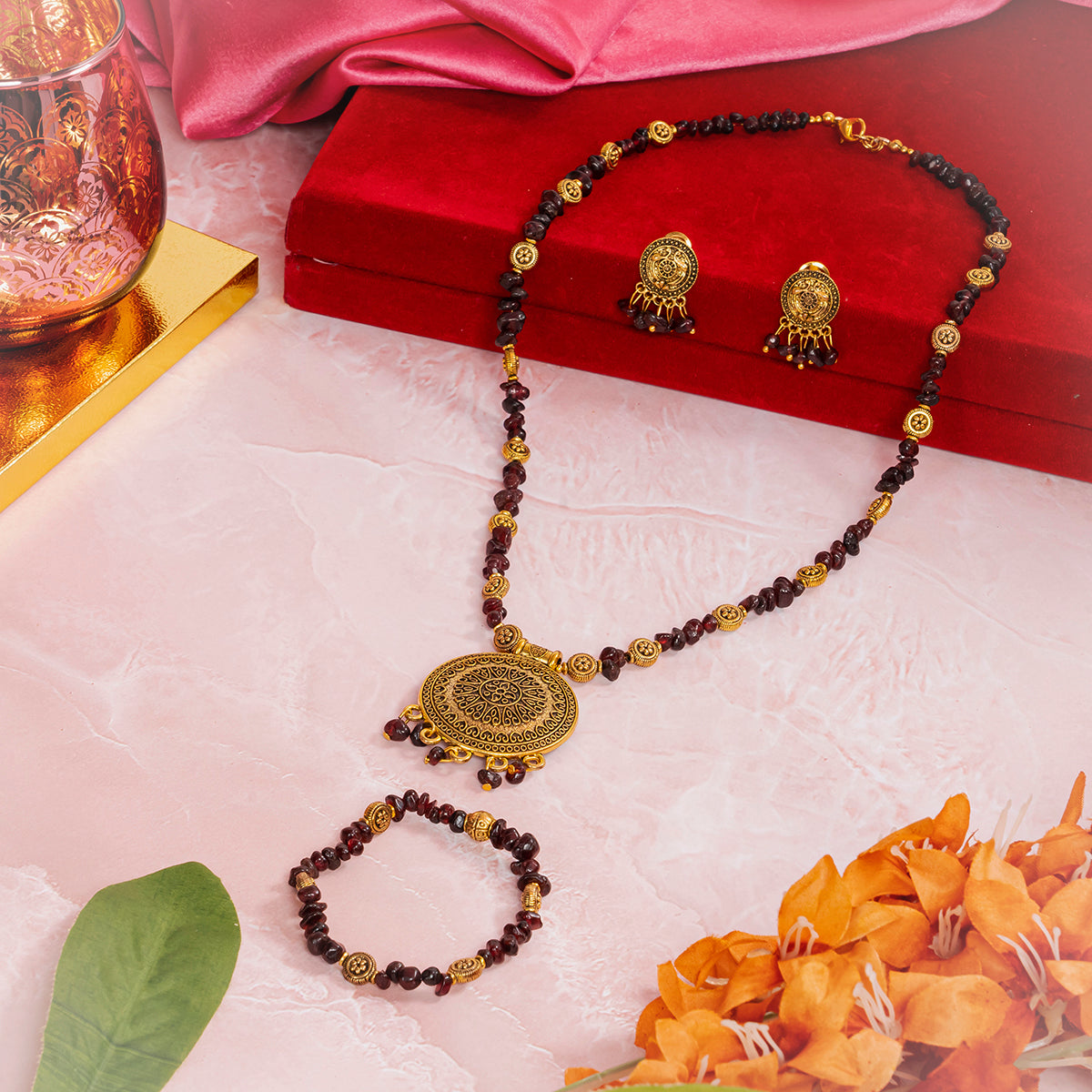 Eykaa jewelry that features garnet semi-precious stone with golden charms set beside red velvet box, pink cloth and flowers