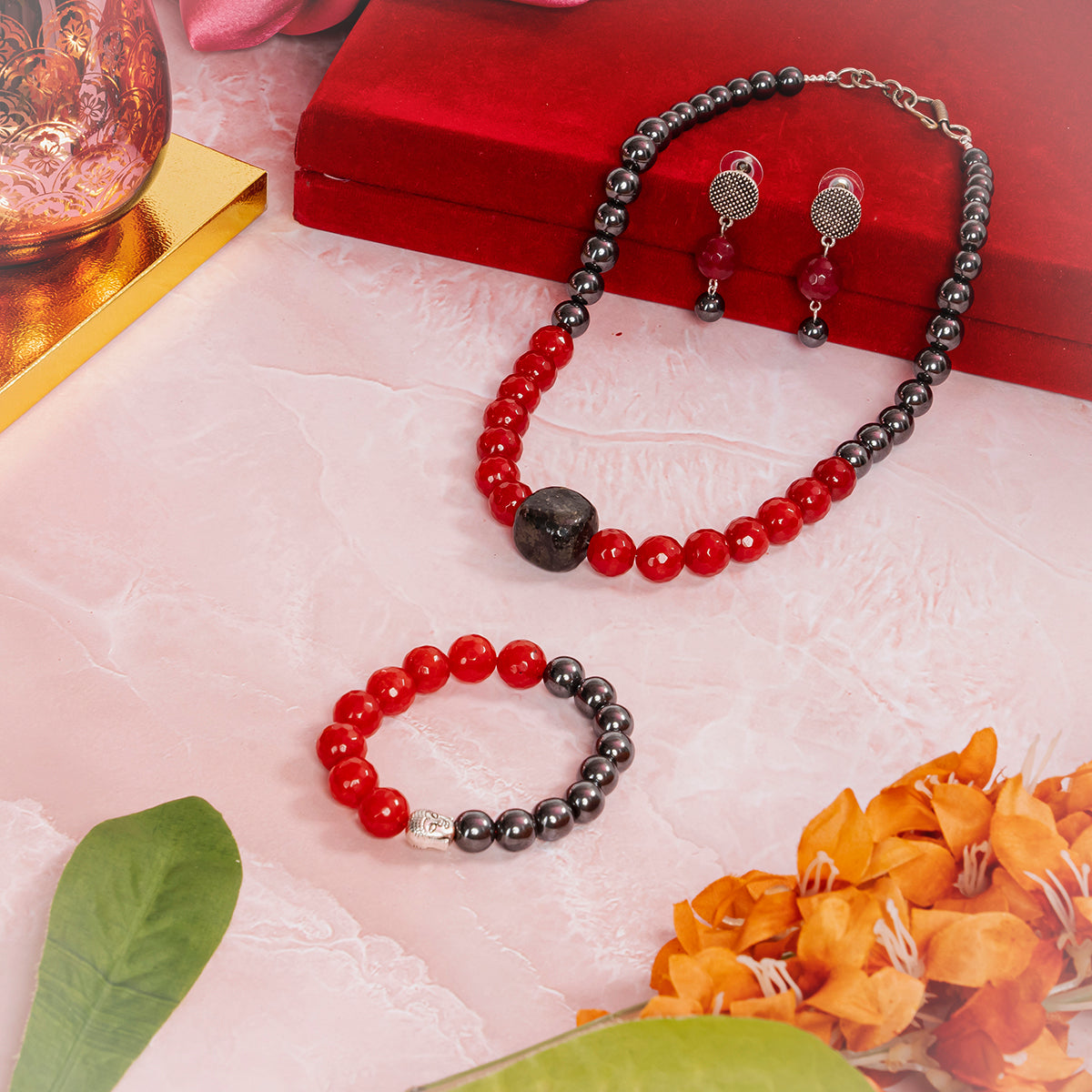 Eykaa Jade With Black Tourmaline And Hematite Necklace With Earrings And A Bracelet On A Pink Marbled Surface, Arranged On And Around A Red Velvet Box, Surrounded By Orange Flowers And Green Leaves.
Eykaa
stone jewellery
womens jewellery
earing for women
bracelet for women
necklace for women
jewellery stores
