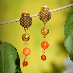 Eykaa earrings that has orange jade, golden lava semi precious stones hanging on a thin branch with green background