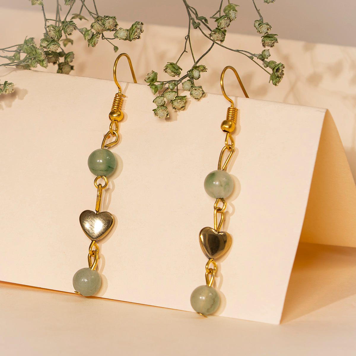 Eykaa green aventurine, golden hematite with golden charms and shell pearls semi precious stone earrings on cream background.
