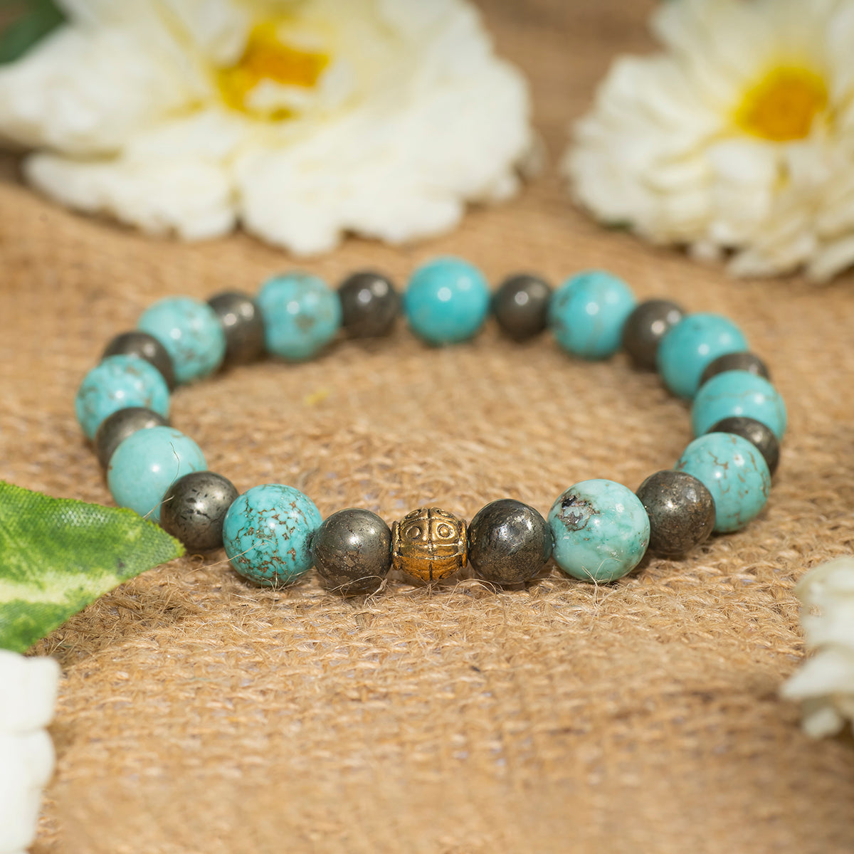 Eykaa EYKAA FIROZA WITH PYRITE AND GOLDEN BEADS BRACELET on sack surface with white flowers.