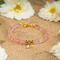 Eykaa cherry quartz with golden charms and shell pearls semi precious stone bracelet on a sack surface with white flowers.