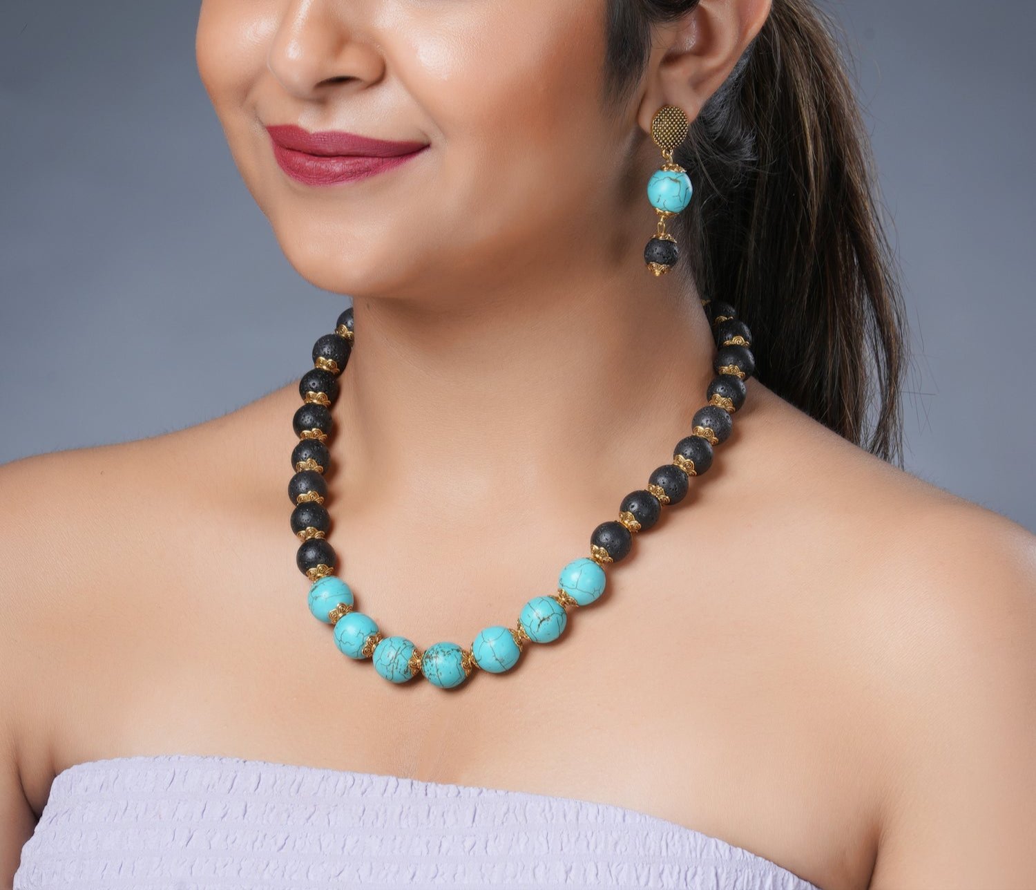 Girl model wearing Eykaa necklace and earrings that features semi precious stone EYKAA FIROZA AND LAVA WITH GOLDEN CHARMS 12 MM AND 14 MM BRACELET