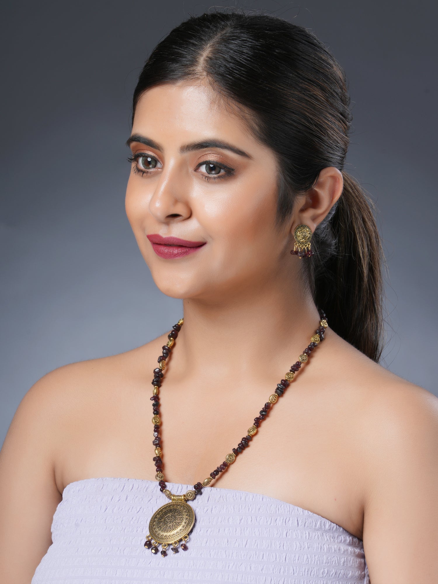 Girl model wearing Eykaa necklace and earrings set that features garnet semi-precious stone with golden charms