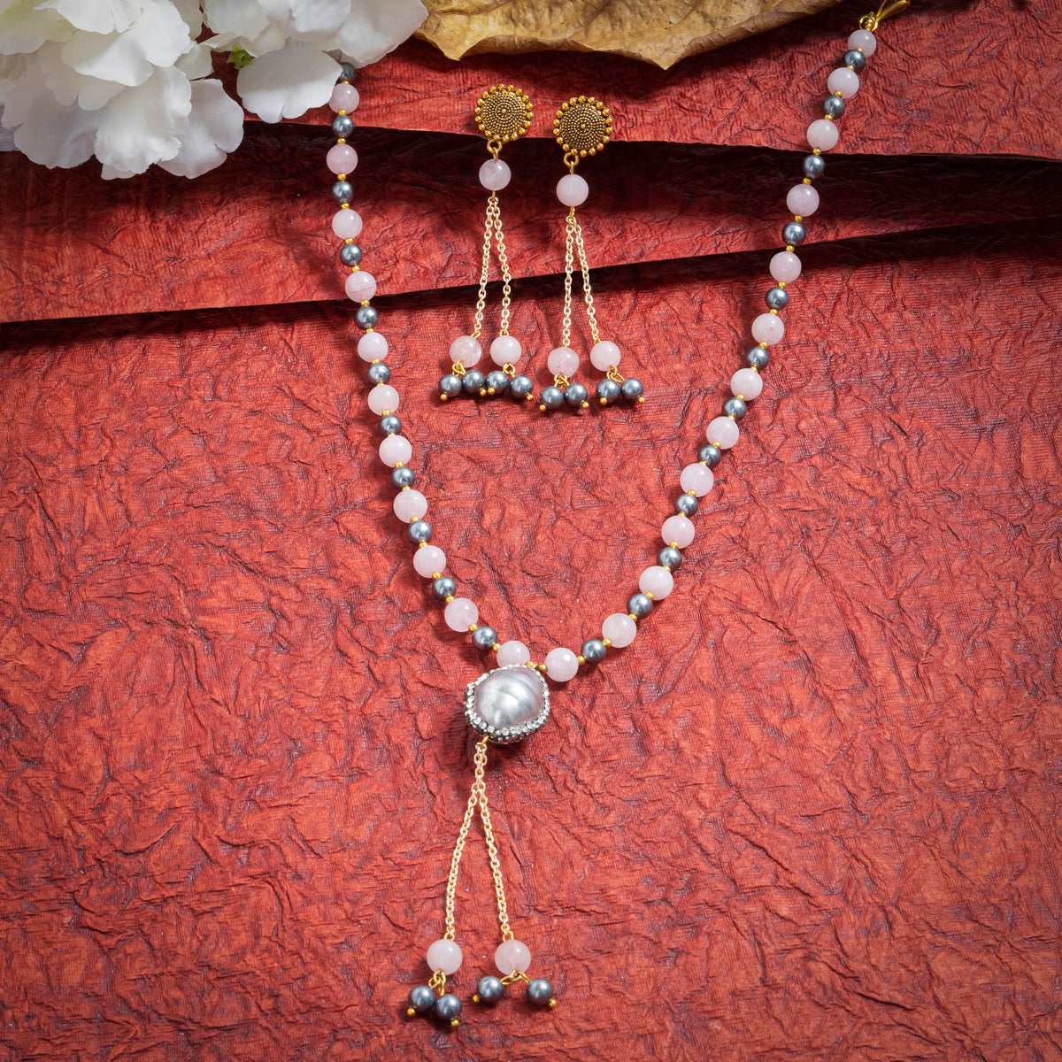 Eykaa Rose Quartz And Shell Pearl Necklace With Earrings On A Textured Red Background With White Flowers.