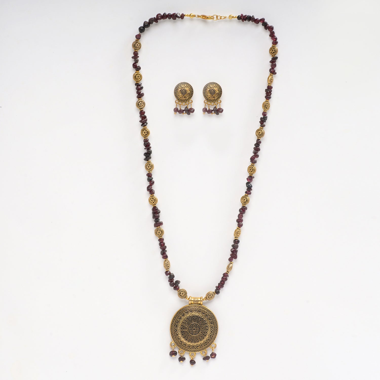 Eykaa necklace and earrings set features garnet semi precious stone with golden charms and pendant on white background.