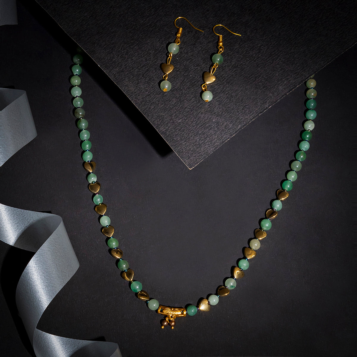 Eykaa green aventurine, golden hematite and shell pearls semi precious stone necklace and earrings on black background.