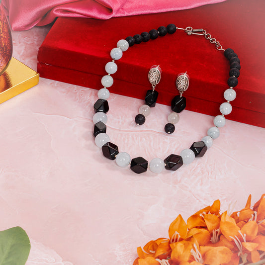 Eykaa  Aquamarine With Lava And Black Onyx Statement Necklace With Earrings And A Bracelet On A Soft Pink Marbled Surface.the Set Is Arranged On And Around A Red Velvet Box, Surrounded By Orange Flowers And Green Leaves.