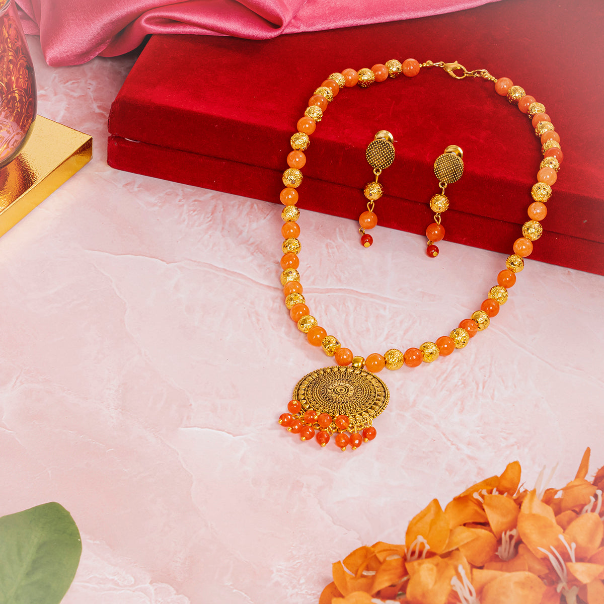 Eykaa necklace, earrings and bracelet feature orange jade with golden lava semi precious stone near red box and pink cloth