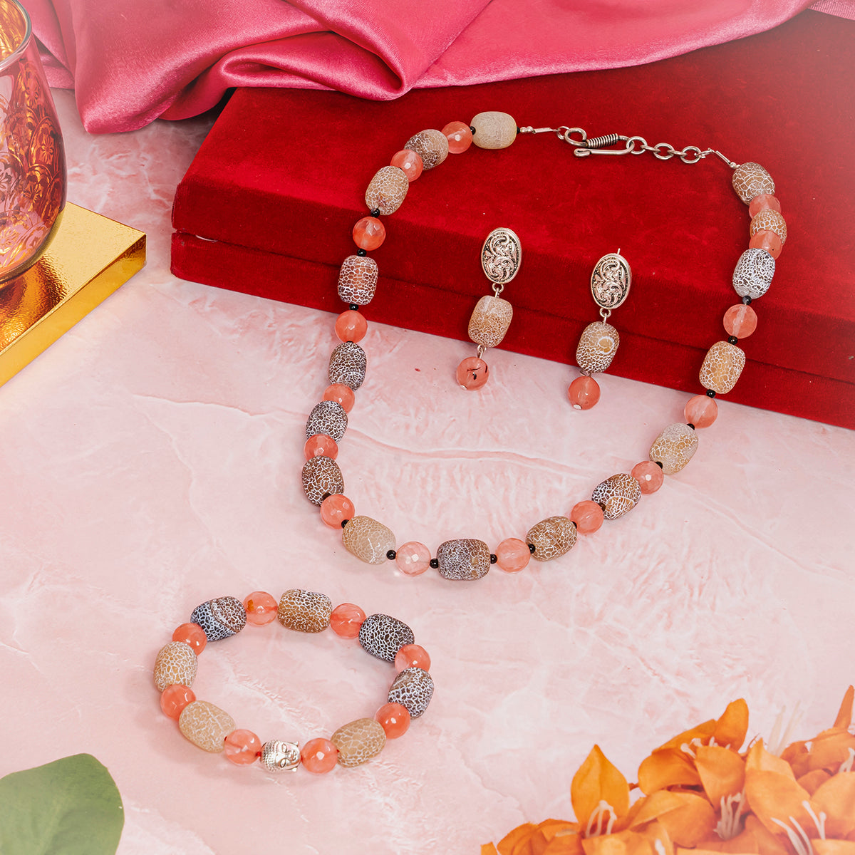 Eykaa jewelry set that have cherry quartz, agate and black onyx semi precious stones over red box, pink cloth and flowers.