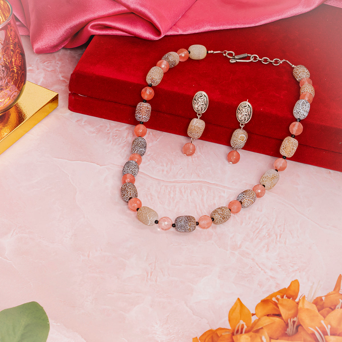 Eykaa jewelry set that have cherry quartz, agate and black onyx semi precious stones over red box, pink cloth and flowers.