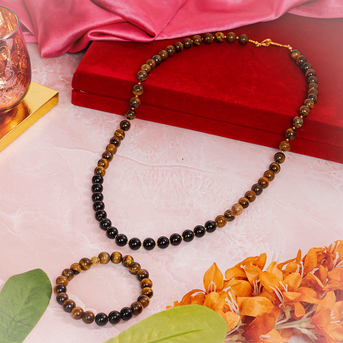 Eykaa brand tiger eye necklace and bracelet set  beside red velvet box, silky pink fabric, and orange flowers