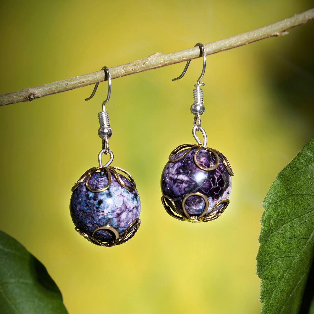 Eykaa jade, kunzite and amethyst semi precious stone earrings with green background hanging on a thin branch. 