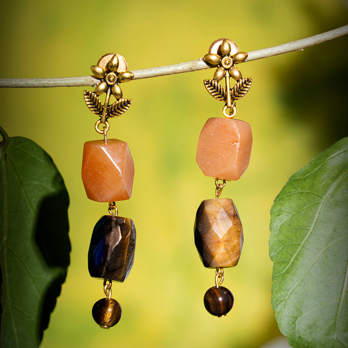 Eykaa tiger eye, hematite with carnelian semi precious stones earrings hanging on a thin branch with green background.Eykaa TIGER EYE AND HEMATITE WITH CARNELIAN NECKLACE