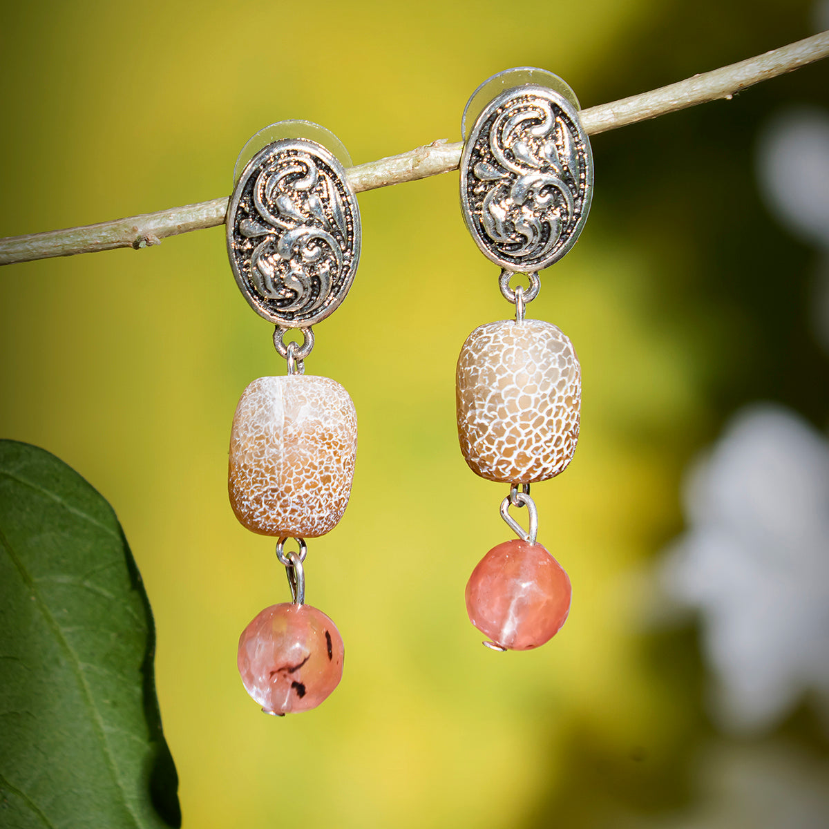 Eykaa earrings that have cherry quartz with agate and black onyx semi precious stones with green background hanging on branch