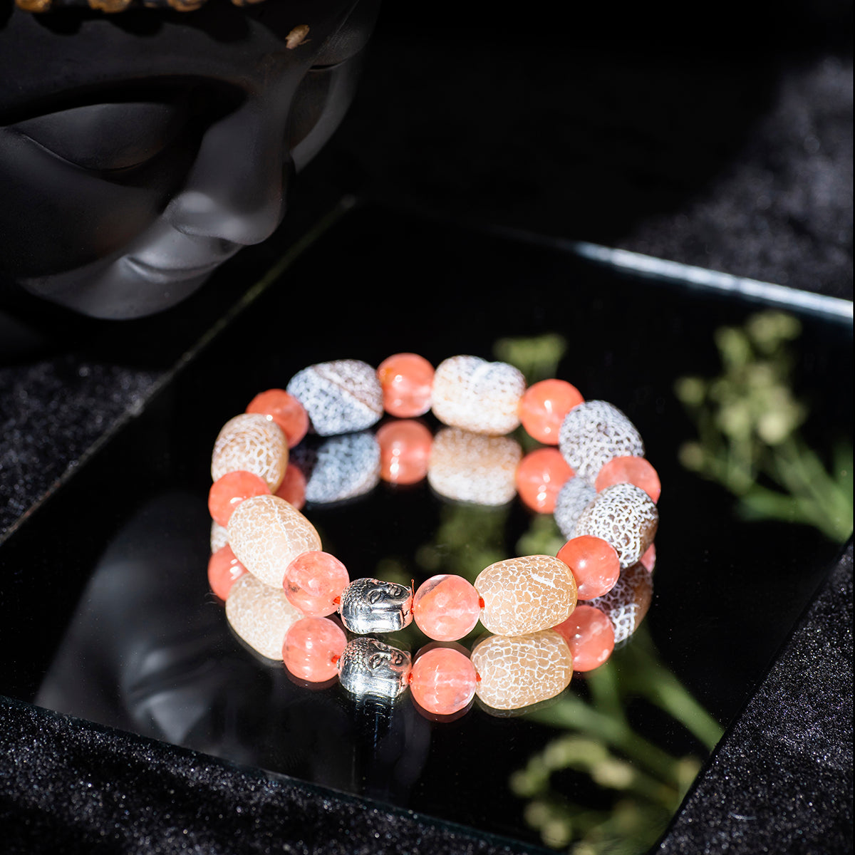 Eykaa bracelet that feature cherry quartz with agate and black onyx semi precious stones on mirror surface beside buddha face