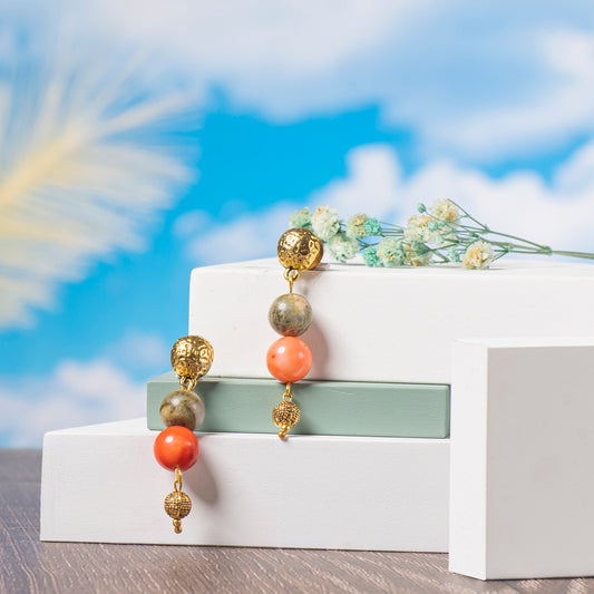 Eykaa Coral And Unakite With Golden Beads Earrings Displayed On Multi-tiered Platform With Sky And Clouds Background.