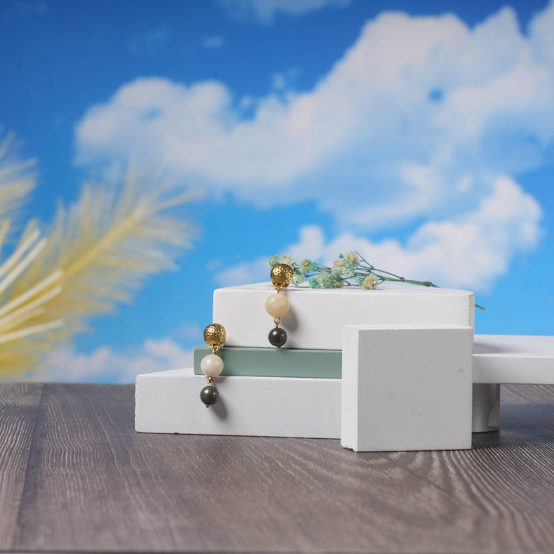 Eykaa Yellow Calcite And Pyrite With Jasper Earrings Displayed On Multi-tiered Platform With Sky And Clouds Background.