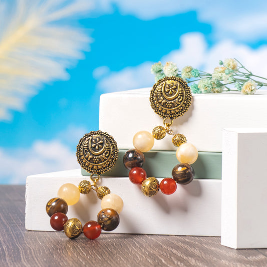 Eykaa Tiger Eye, Yellow Calcite And Red Onyx With Yellow Aventurine Earrings Displayed On Multi-tiered Platform With Sky And Clouds Background.