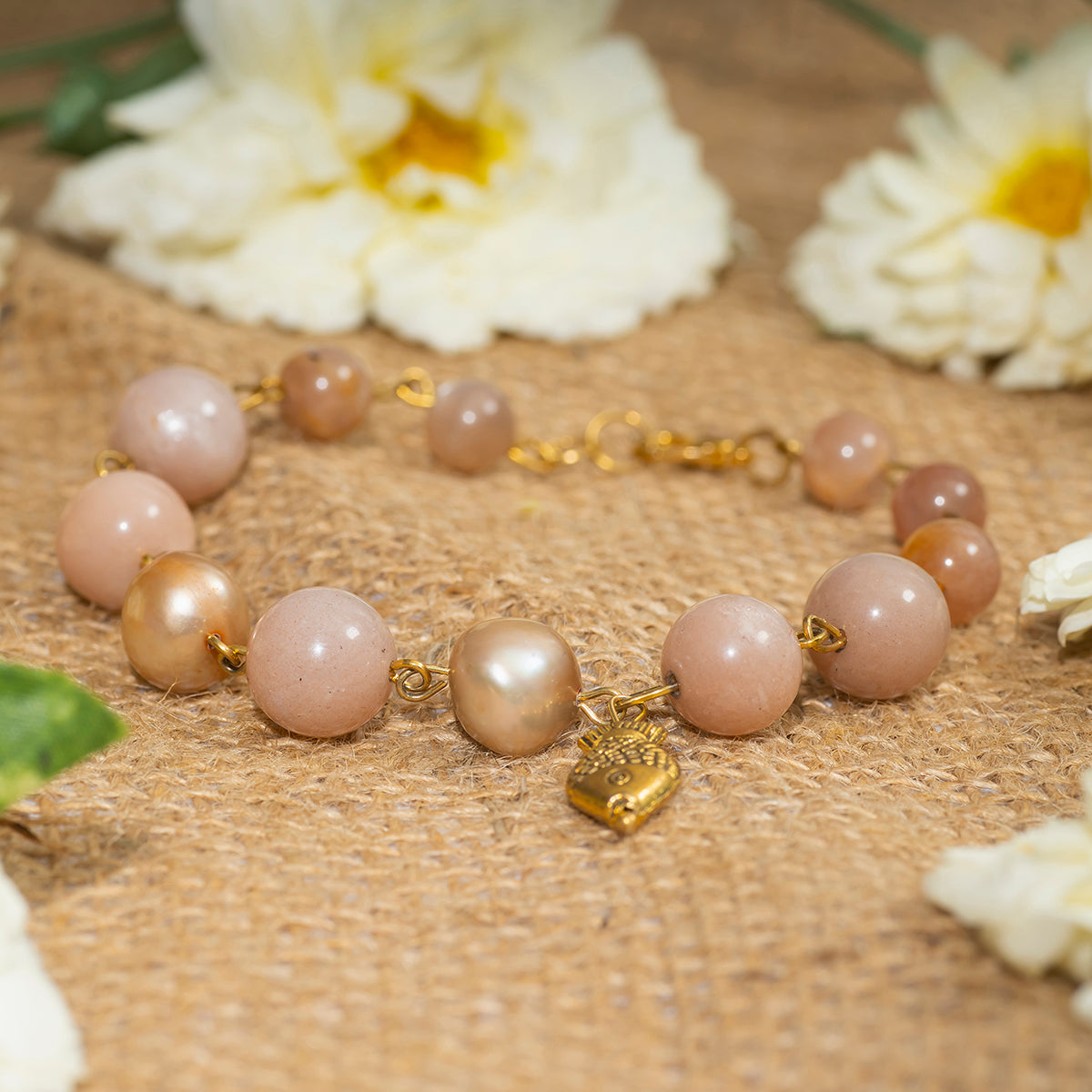 Eykaa peach moonstone with freshwater pearl and shell pearls semi precious stone bracelet on a sack surface and white flowers