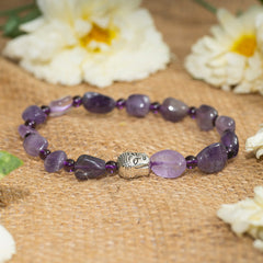 Eykaa amethyst tumble layered semi precious stone bracelet on a sack surface with beautiful white flowers beside. 