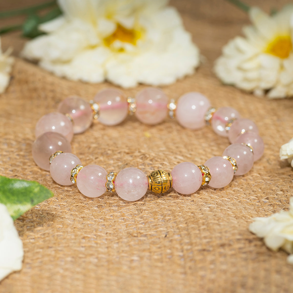 Eykaa eykaa rose quartz with golden diamond charms bracelet on sack surface with white flowers.