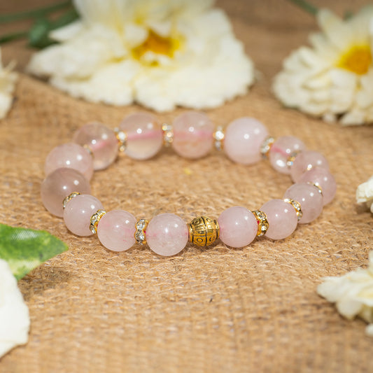 Eykaa eykaa rose quartz with golden diamond charms bracelet on sack surface with white flowers.