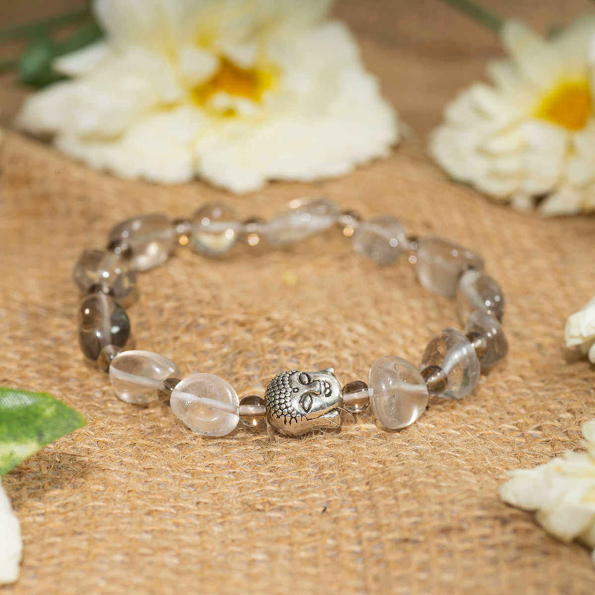 Eykaa EYKAA SMOKEY QUARTZ TUMBLE LAYERED BRACELET on sack surface with white flowers.