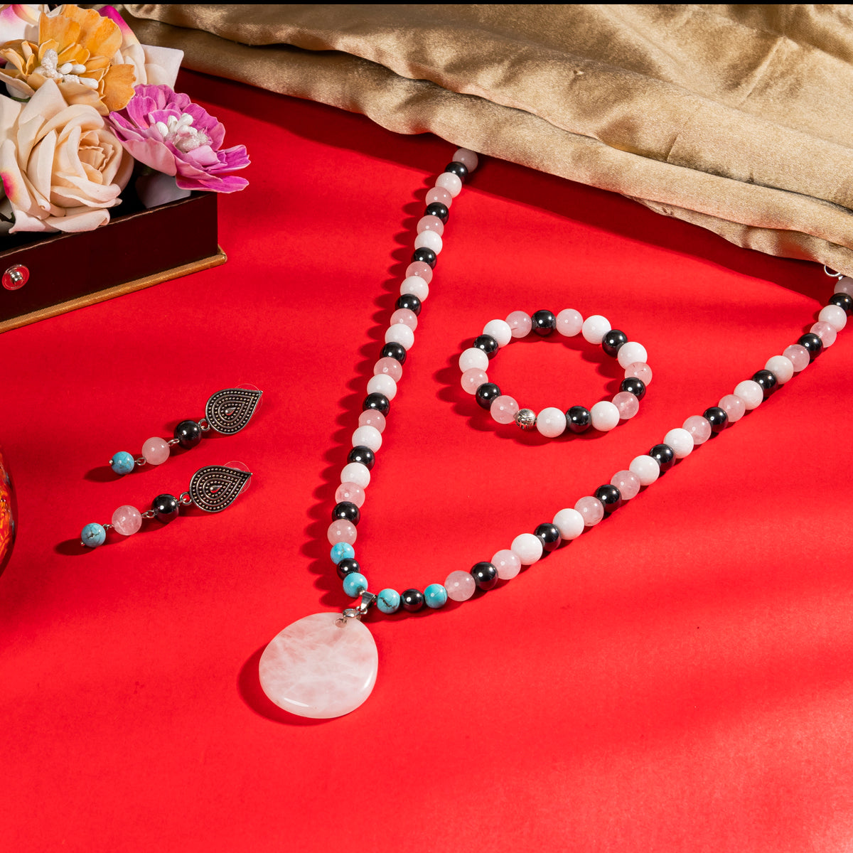 Eykaa Rose Quartz, Hematite, Marble, Firoza Necklace with Rose Quartz Pendant, Earrings And Bracelet On A Vibrant Red Surface.