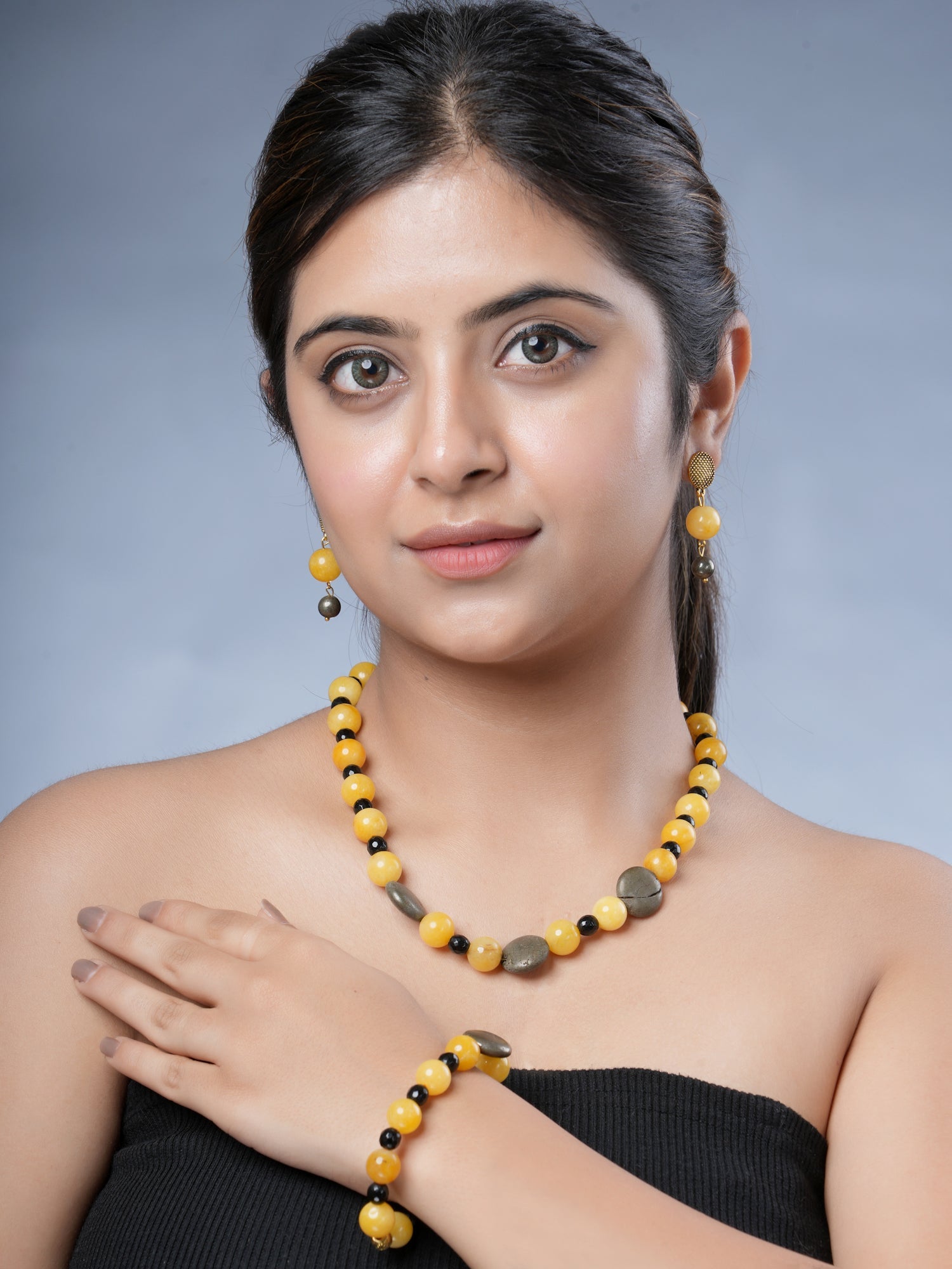 Girl model wearing Eykaa necklace, earrings and bracelet that has yellow jade, pyrite and black jade semi-precious stone.