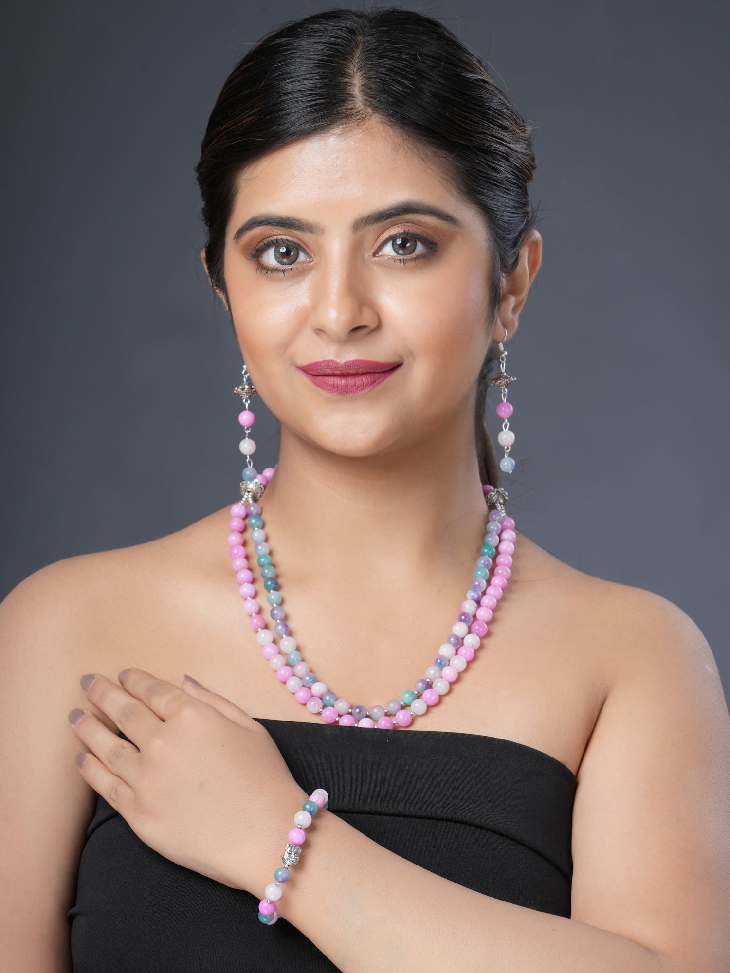 Girl model wearing Eykaa layered necklace, earrings and bracelet that feature pink and multicoloured semi precious stone jade. 