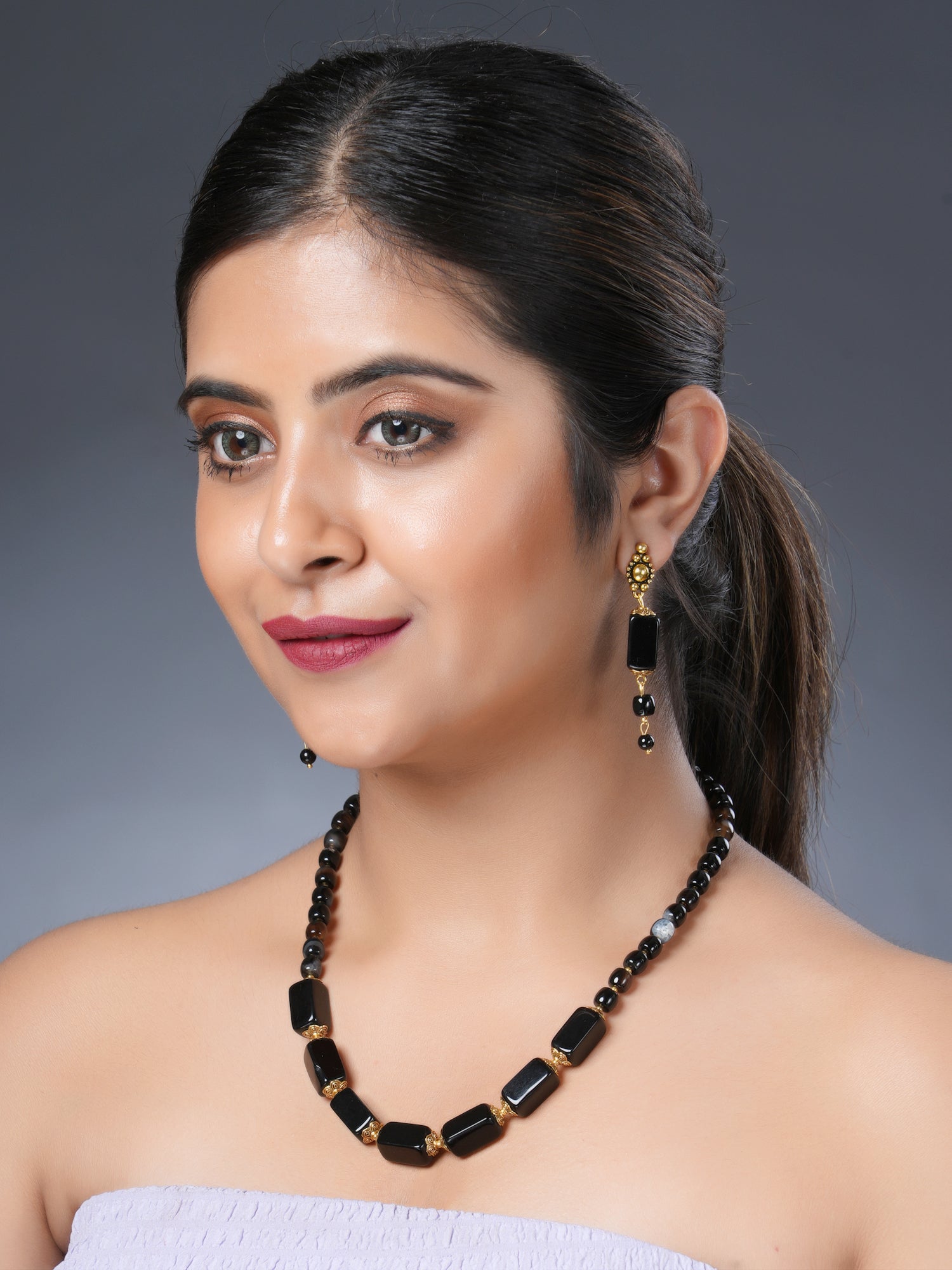 Girl model wearing Eykaa necklace and earrings that feature semi-precious stone black onyx with hakik and golden charm. 