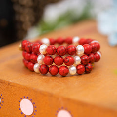 Eykaa Red Howlite And Freshwater Pearl Bracelet Displayed On A Textured Orange Surface.