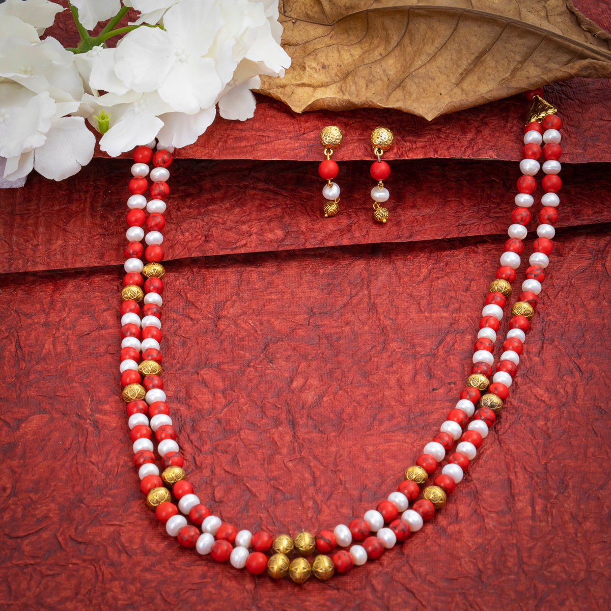 Eykaa Red Howlite And Freshwater Pearl Necklace With Earrings On A Textured Red Background With White Flowers.