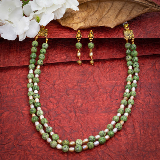 Eykaa Green Dalmatian And Fresh Water Pearl Necklace With Earrings On A Textured Red Background With White Flowers.