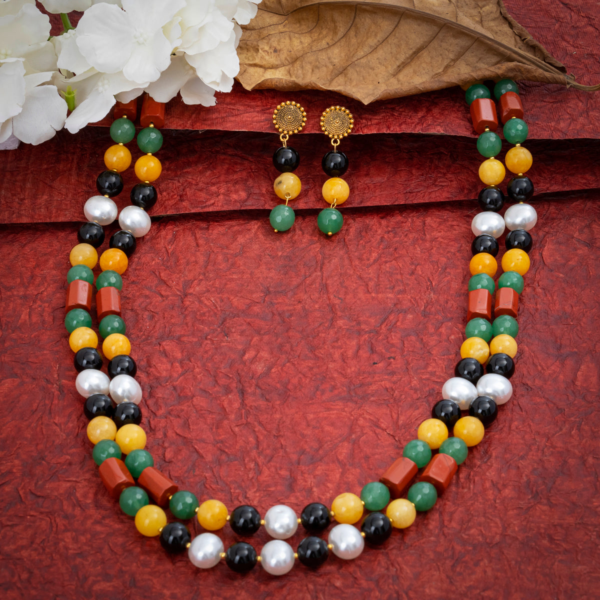 Eykaa Black Onyx, Red Jasper, Green Jade And Yellow Jade With Korean Pearl Ball Necklace With Earrings On A Textured Red Background With White Flowers.