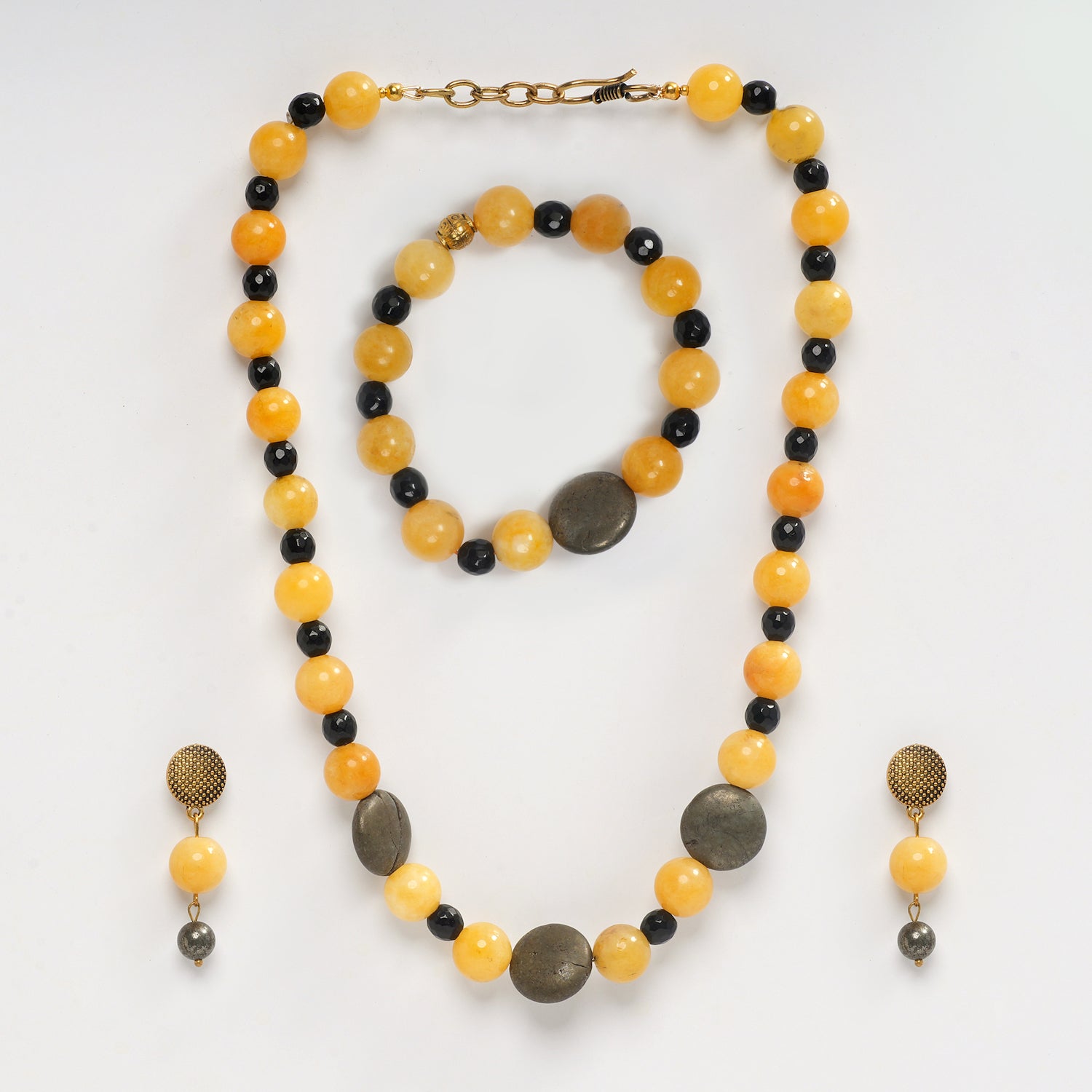 Eykaa yellow jade, pyrite coins and black jade semi precious stone necklace, earrings and bracelet on a white background.